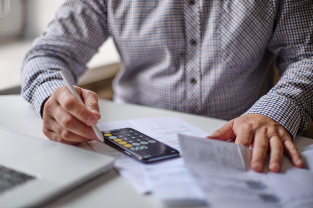 Man with smartphone examining bills, documents or receipts at home 