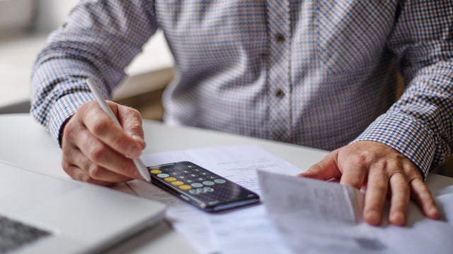 Man with smartphone examining bills, documents or receipts at home 