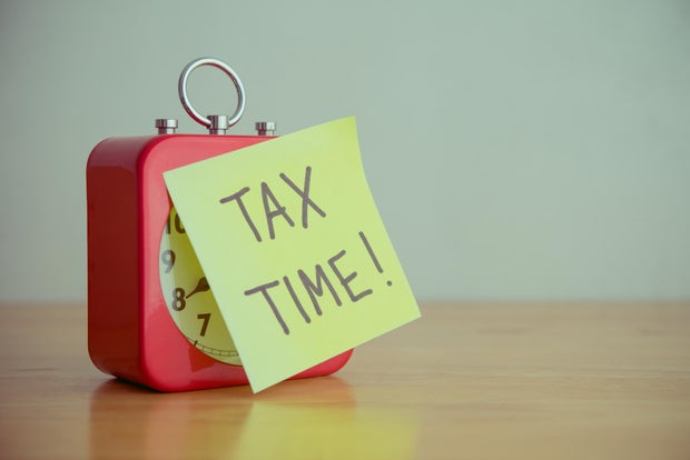 Red alarm clock with TAX TIME paper note on wooden table white wall background copy space. 