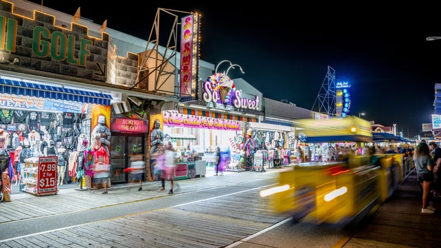 People are on the boardwalk in Wildwood after dark as the tram car goes by 