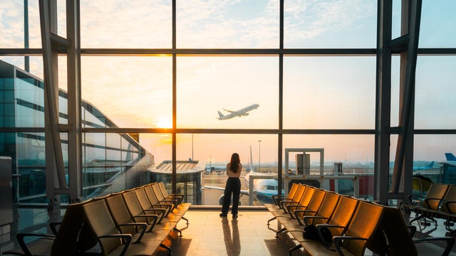A young Asian woman is using a smartphone to check the arrival departure board and flight schedule at the airport. 