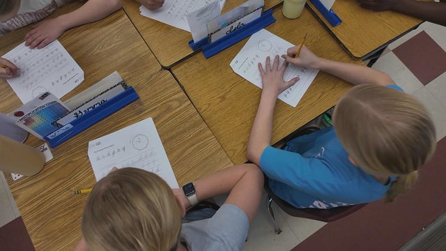 Students work at their desks on cursive worksheets 