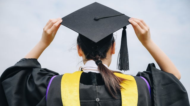 Rear view of young student wearing graduation gown with graduation cap in her commencement day. 
