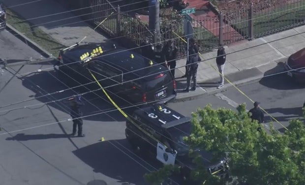 Officers seen standing near an unmarked police vehicle that has several crime scene markers on its hood 