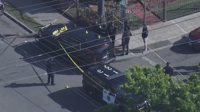 Officers seen standing near an unmarked police vehicle that has several crime scene markers on its hood 