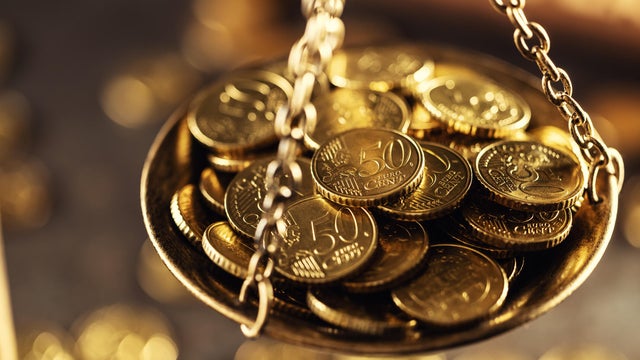 Antique brass scales, one pan filled with gold coins, tilted towards wealth. In the blurred background, a wooden gavel and other coins are present, evoking the theme of justice, law and money. Close-up 