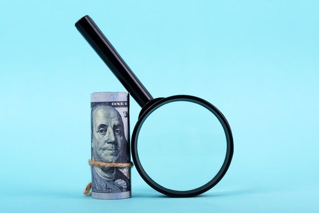 Magnifying Glass and Money Roll on Blue Background 