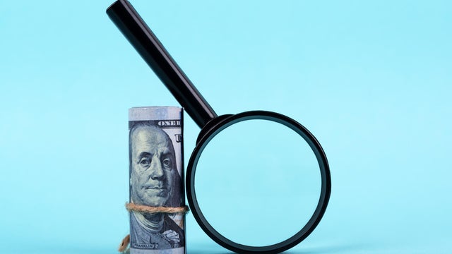 Magnifying Glass and Money Roll on Blue Background 