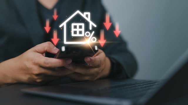 Businessman use smartphone with virtual home icon and down arrow for economical real estate and lower mortgage interest rates. Reduced prices for rental housing, Demand for home purchases decreases. 