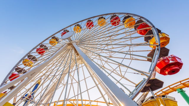 Low angle view of multi-coloured vibrant ferris wheel against blue sky 