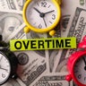 Alarm clock and sticky note with the word OVERTIME on a one hundred dollars 