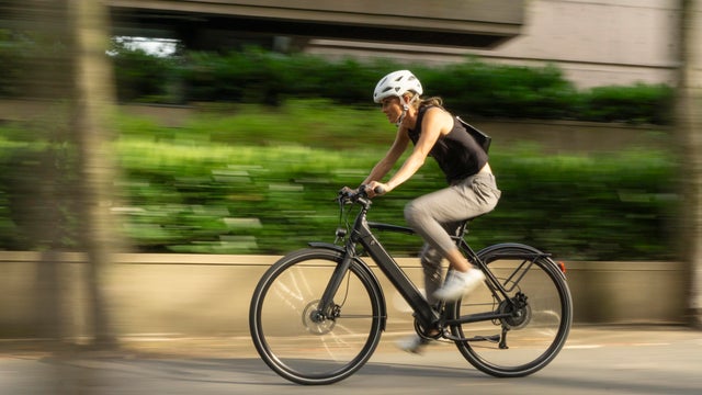 a woman bicycle riding commuting in the city of Vancouver on an ebike with a battery powered commuter bike through the city of vancouver, gastown, stanley park with views of downtown city skyline. 