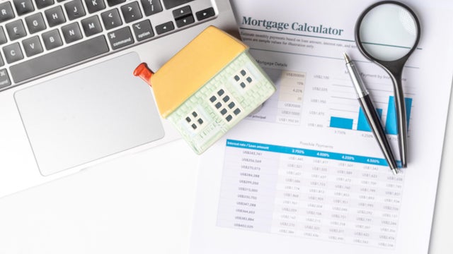 Calculating mortgage options and financial planning with a calculator, laptop, and house model at a workspace 