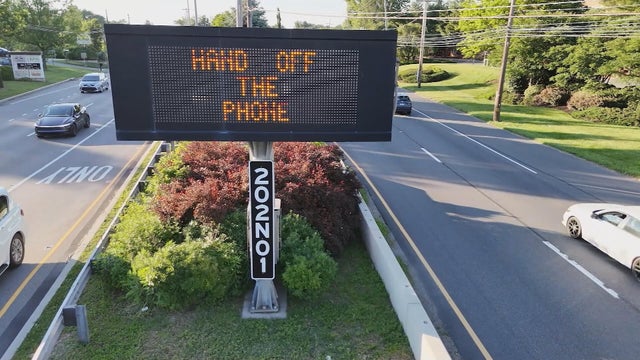 A roadside sign says Hands Off The Phone 