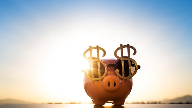 Piggy bank wearing sunglasses with dollar money sign against sunset sky background 