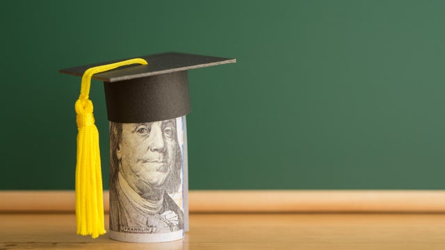 US dollars banknote wears graduation cap chalkboard background in classroom. 