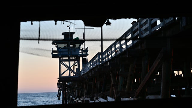 Silhouette of a pier and lifeguard stand against a serene sunset sky over the ocean, viewed through a dark frame 
