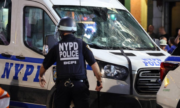 A NYPD officer walks by a damaged police vehicle as crowds of New York Knicks fans become restless outside Madison Square Garden after their team's Game 4 victory over the San Antonio Spurs in the NBA Finals in New York on June 10, 2026.