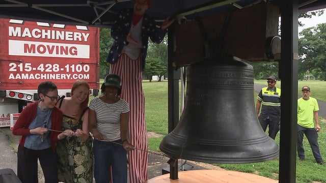 Three people work together to ring a replica Liberty Bell 