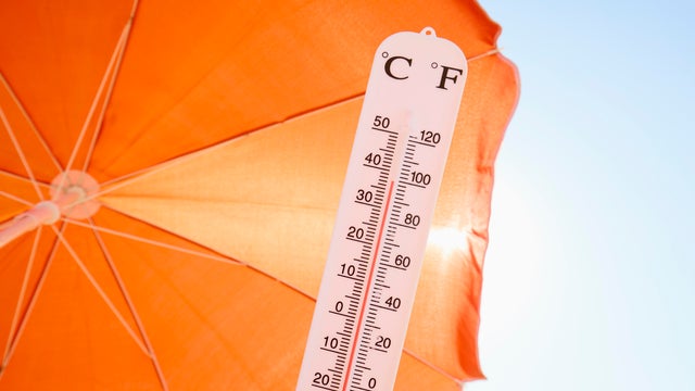 Thermometer against orange parasol, sky and sun 