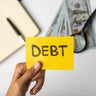 Hands Holding "DEBT" Label with Financial Tools and Money 