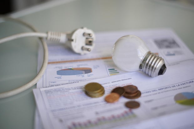 An electricity bill on a table with a cable and plug, a light bulb, and coins