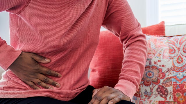 Woman Sits on Couch With Abdominal Pain 