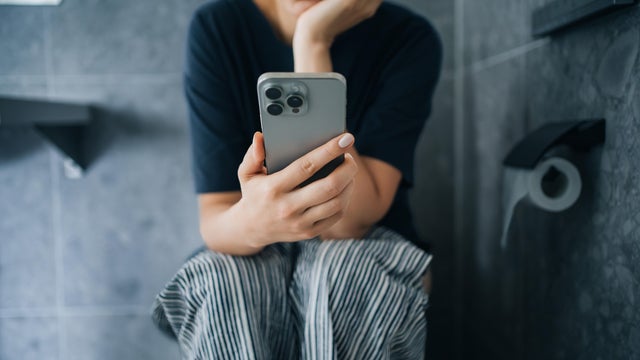 Cropped shot of young Asian woman using smartphone while sitting on toilet in bathroom. Daily routine. Lifestyle and technology 