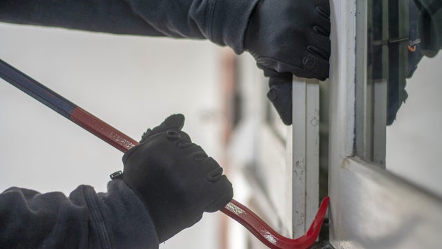 Burglar with crowbar trying break the door to enter the house 