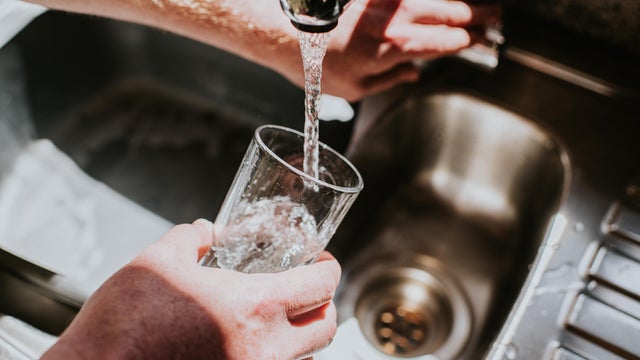 A man pours a glass of water from a chrome tap at a kitchen sink 
