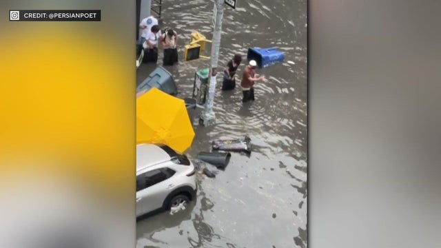 People wearing trash bags walk through flooded street 