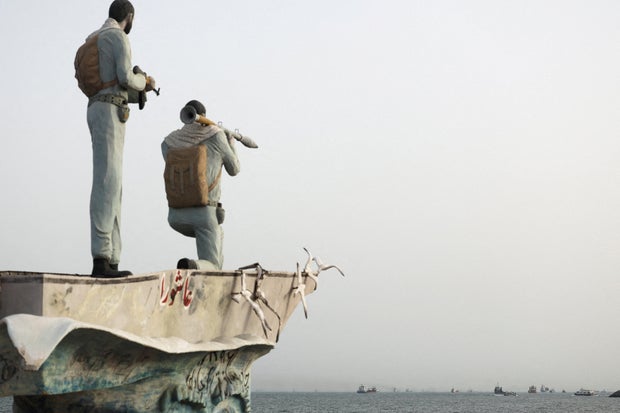  A statue of Iranian military members stands as vessels in the Strait of Hormuz are visible near the beach of Bandar Abbas 