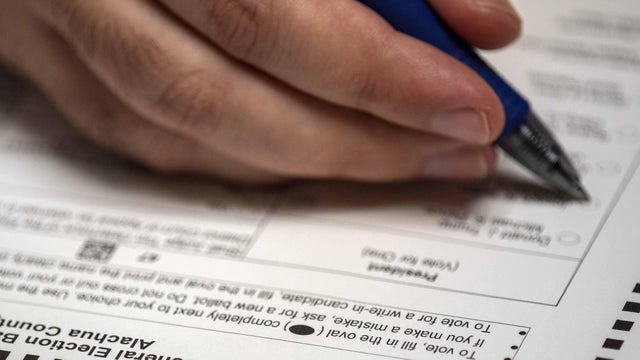 Absentee ballot form with pen in hand filling in bubble 