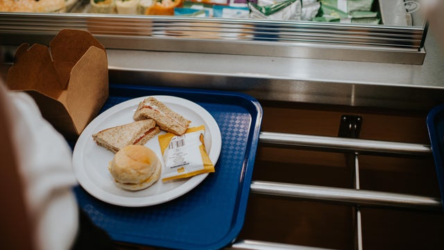 High school pupils in a cafeteria add their choice of food onto plates on blue trays during lunch break in a school. 