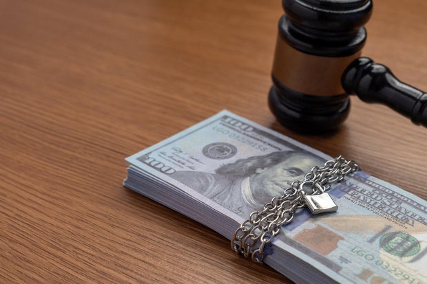 A judge's gavel next to a stack of money bound by a metal chain and secured with a padlock.