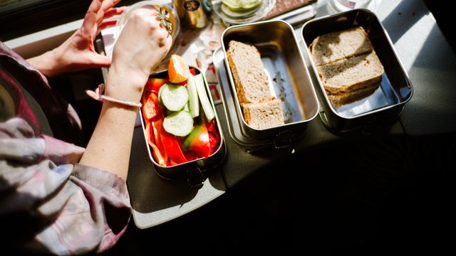 Woman Eating Healthy Packed Lunch With Sandwiches And Fresh Vegetables In Metal Lunchboxes 