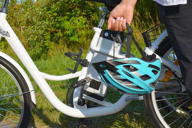 Women with helmet stand near electric bicycle in the park in sunny summer day. The view of the e bike battery pack. Unfiltered, with natural lighting.