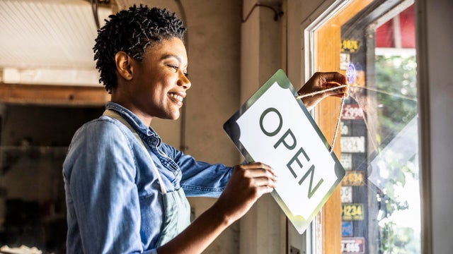 Female small business owner placing open sign in business window 