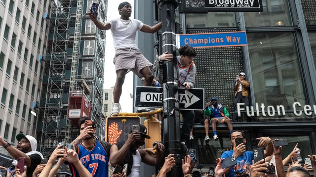 Fans climb a lamp post near a sign renaming Broadway as "Champions Way" during the New York Knicks Championship ticker tape parade and victory rally celebrating winning the 2026 NBA Finals on June 18, 2026 in New York City. 