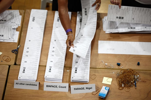 A counter adds a ballot paper to the pile of votes for Reform U.K.'s candidate Nigel Farage at Clacton Leisure Centre, eastern England, on Aug. 14, 2026. 