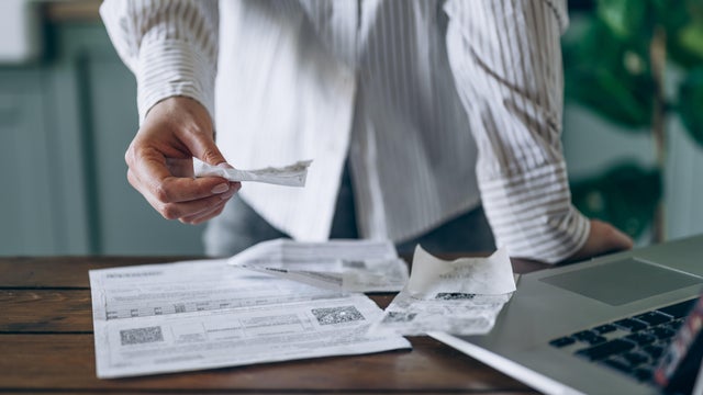 Woman Reviews Receipts at Kitchen Table 
