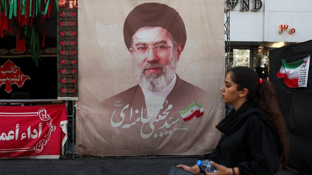 A woman walks next to a banner with a picture of Iran's Supreme Leader Mojtaba Khamenei in Tehran 