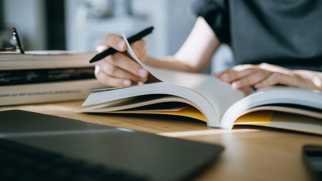 Close up. mid-section of young Asian woman reading book and making notes at home, concentrates on her studies. Further education concept 