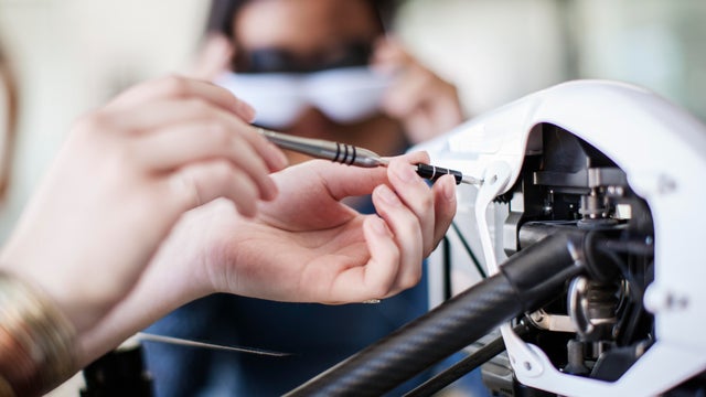 Cropped image of female student working on drone with friend in background 