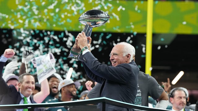 Jeffrey Lurie holds up the Vince Lombardi trophy as green and white confetti falls in the background and the Eagles cheer 