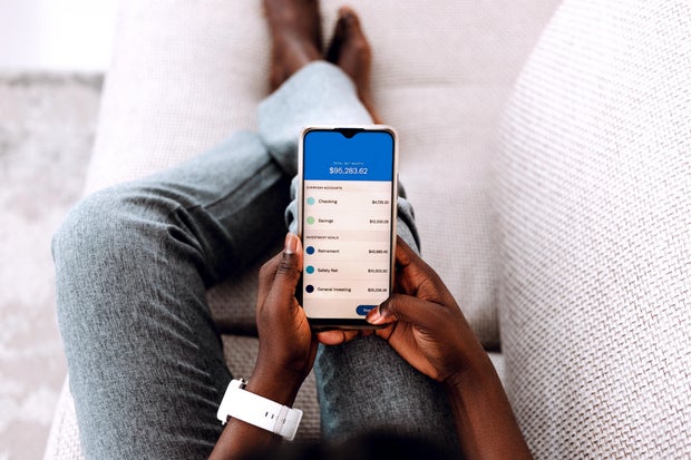 Overhead view of young Black woman managing online banking with smartphone sitting on the sofa at home. 