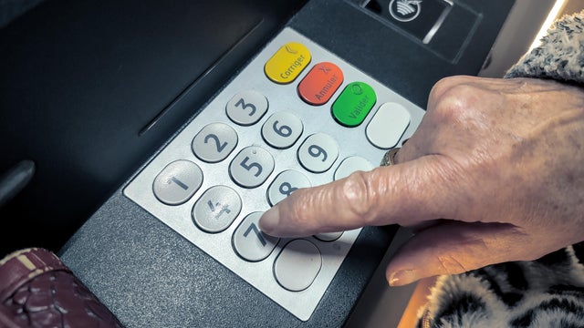 Elderly person entering a PIN on payment terminal, highlighting fraud risk, card scam, and financial crime targeting vulnerable users. 