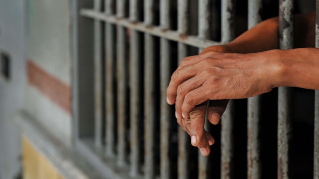 prisoner's hands behind bars with black background 
