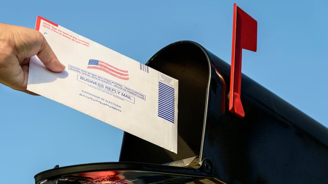 Woman's hand placing a 2020 mail-in election ballot in a rural mailbox 