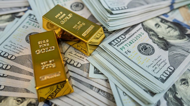 Shiny gold bullion bars on hundred dollar banknotes representing luxury, savings and financial stability 